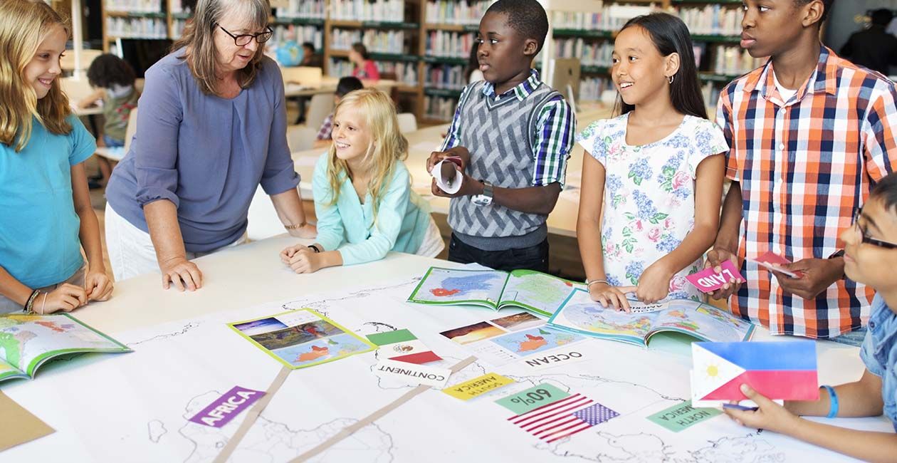 6 students and a teacher around a table with maps and flags of different countries 